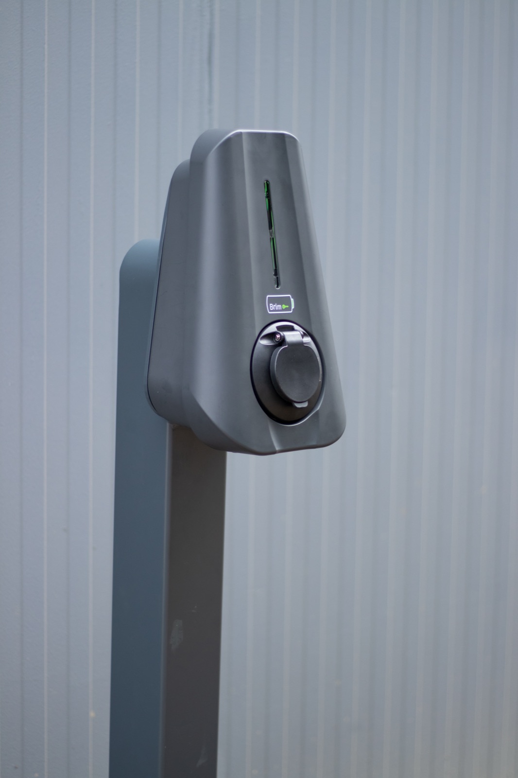 A Brim 7.4kW charger wall mounted on grey cladding, its status light lit