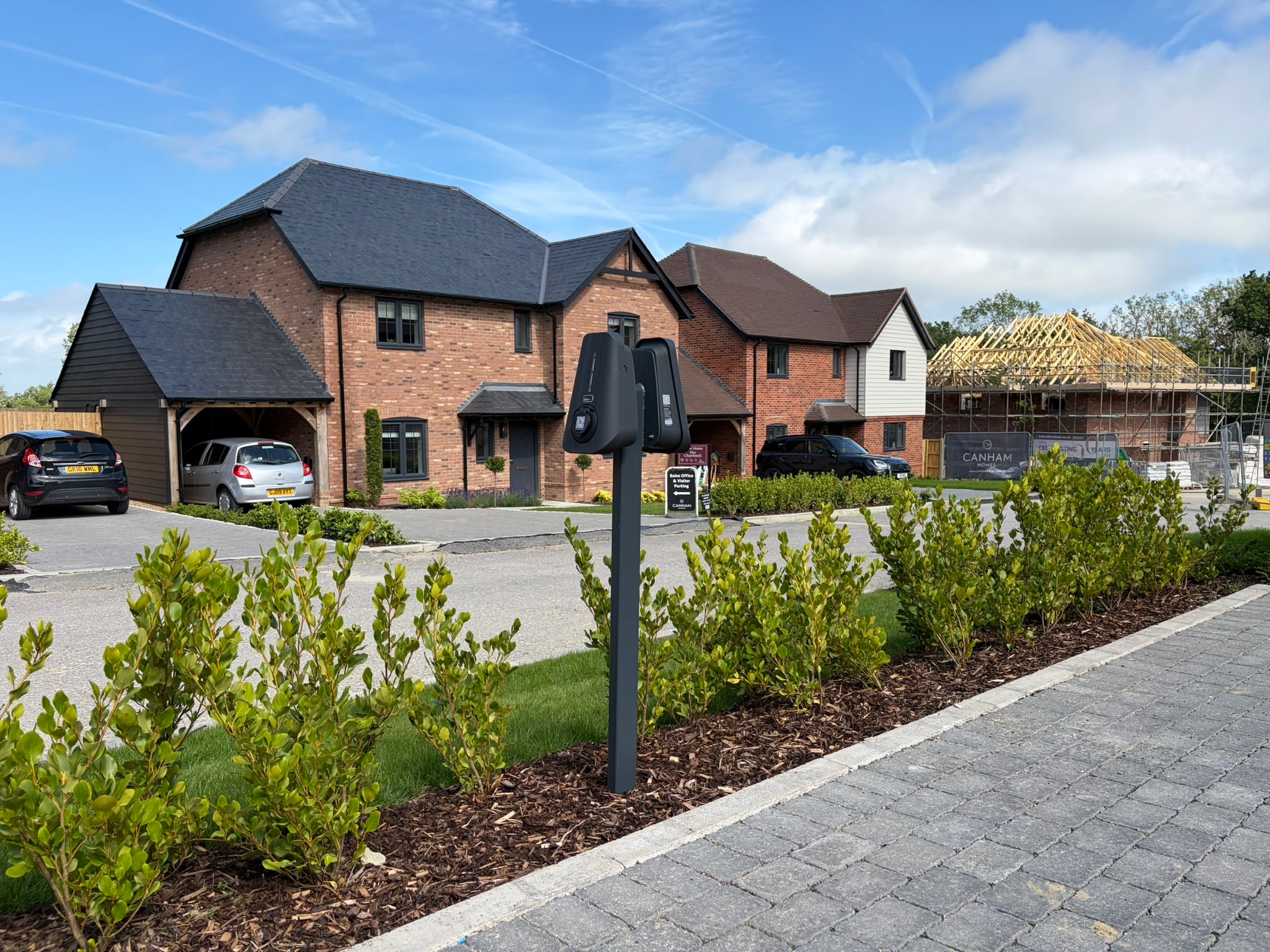 A Brim dual charger post beside the road on a new-build development, with the next homes still in scaffold behind it